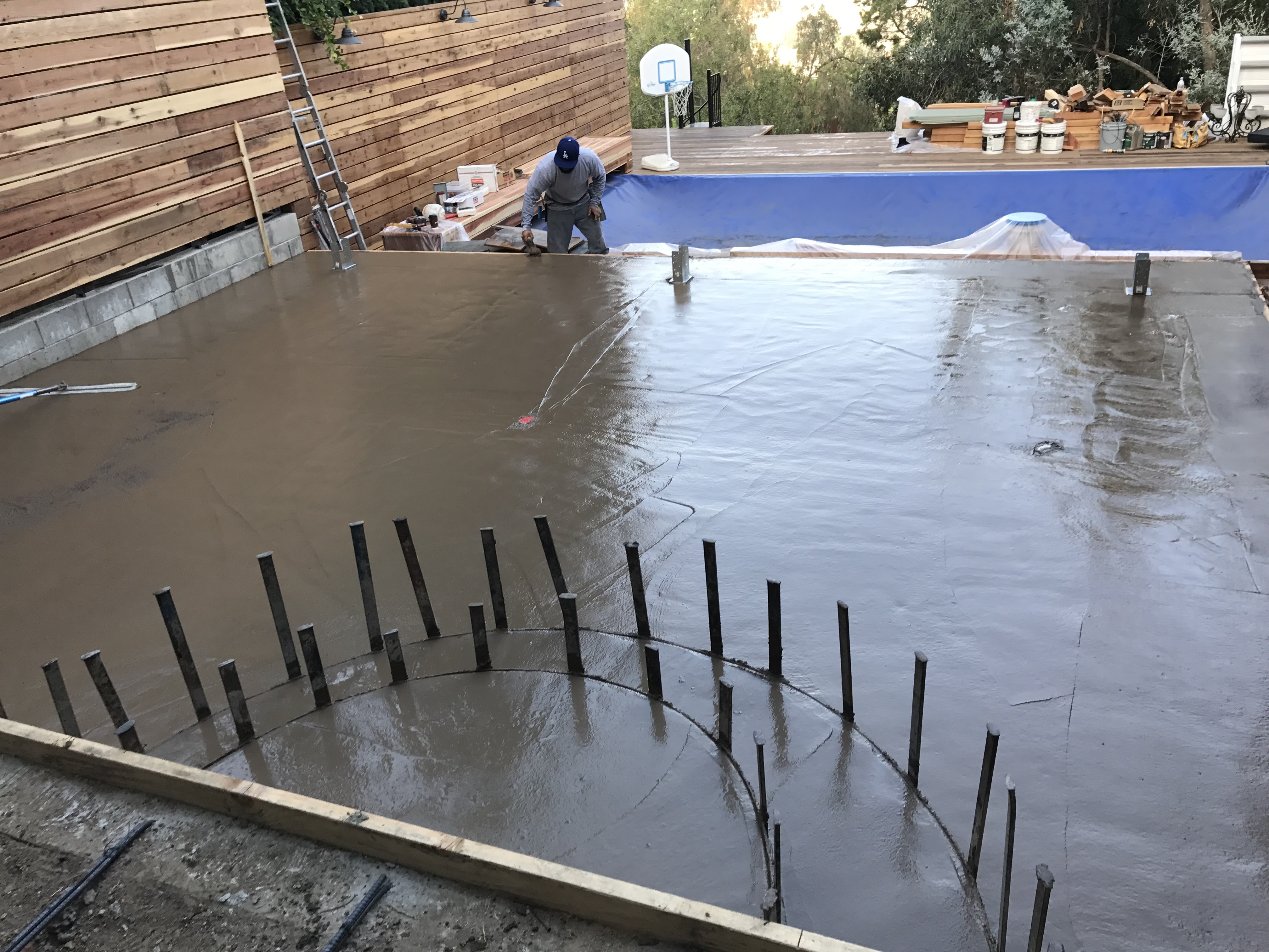 Image 5: A smooth wet concrete slab.  It has 2 semi circles of rebar sticking out of the front of the slab that looks like they will be used for stairs.